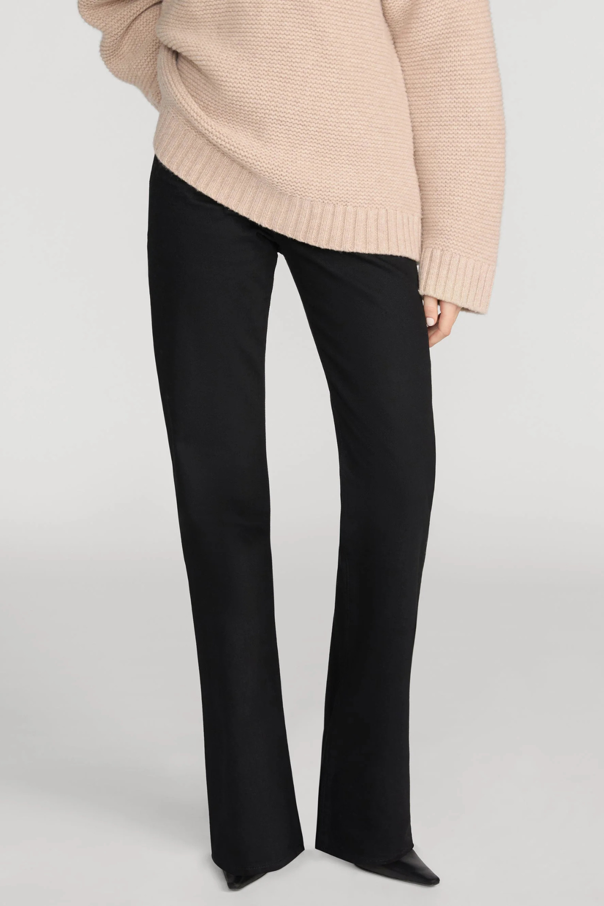 A model wearing black wide-leg trousers and a beige ribbed knit sweater, shown from the chest down against a light gray studio background.