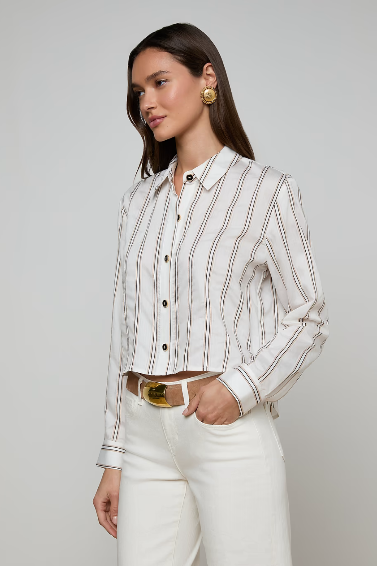 Woman wearing a white striped shirt and white pants on a gray background