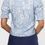 Person wearing a light blue floral blouse with navy shorts on a white background