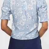 Person wearing a light blue floral blouse with navy shorts on a white background