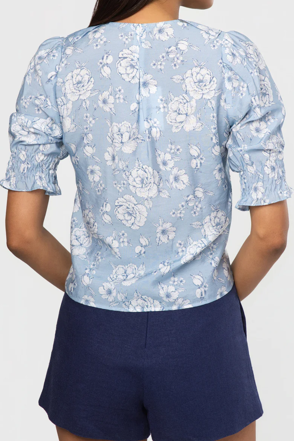 Person wearing a light blue floral blouse with navy shorts on a white background
