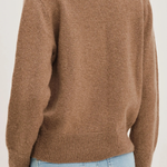 A person shown from the back wearing a soft knit sweater in a warm taupe-brown color, paired with light blue jeans, against a plain light background.