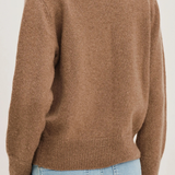 A person shown from the back wearing a soft knit sweater in a warm taupe-brown color, paired with light blue jeans, against a plain light background.