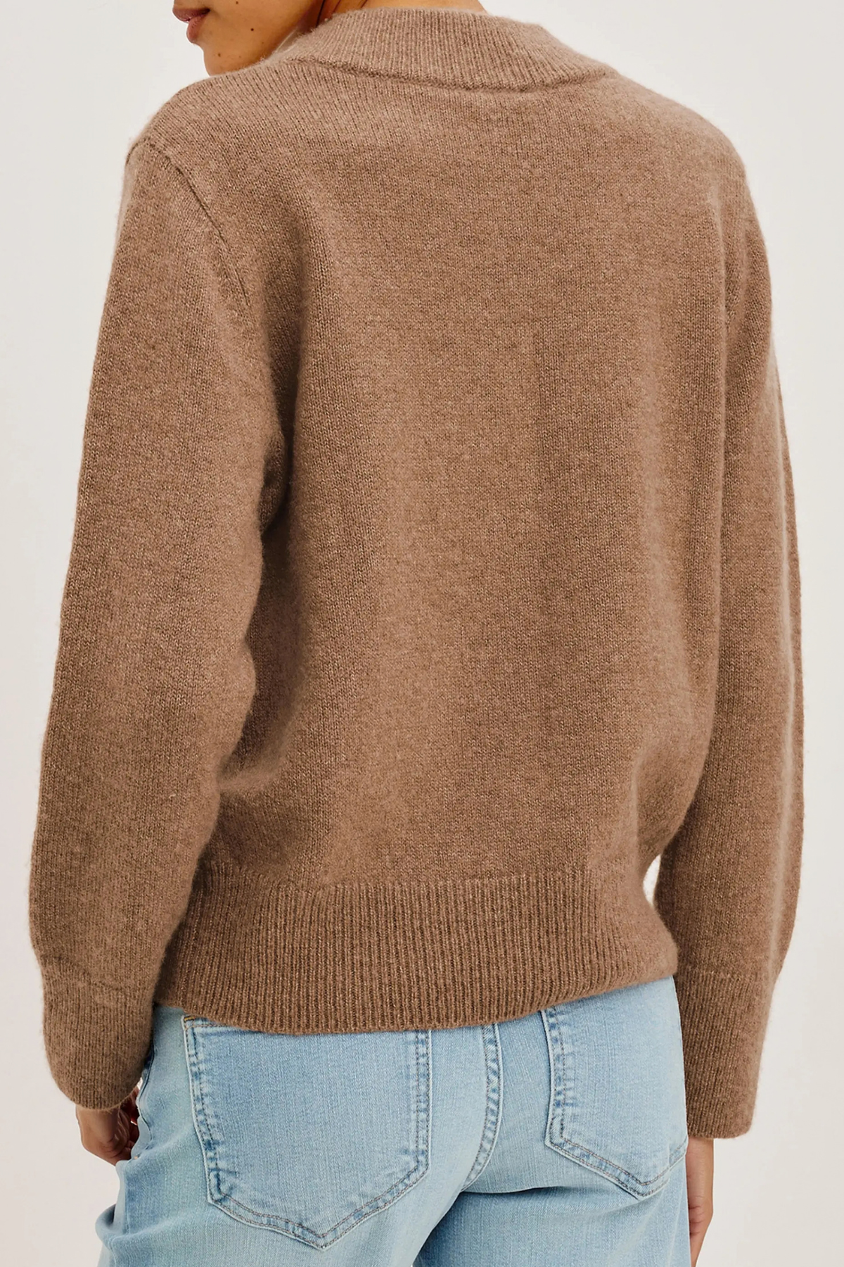 A person shown from the back wearing a soft knit sweater in a warm taupe-brown color, paired with light blue jeans, against a plain light background.