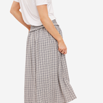 A woman shown from the back wearing a white short-sleeve top, a high-waisted beige and gray plaid midi skirt, and tan boots against a plain light background.