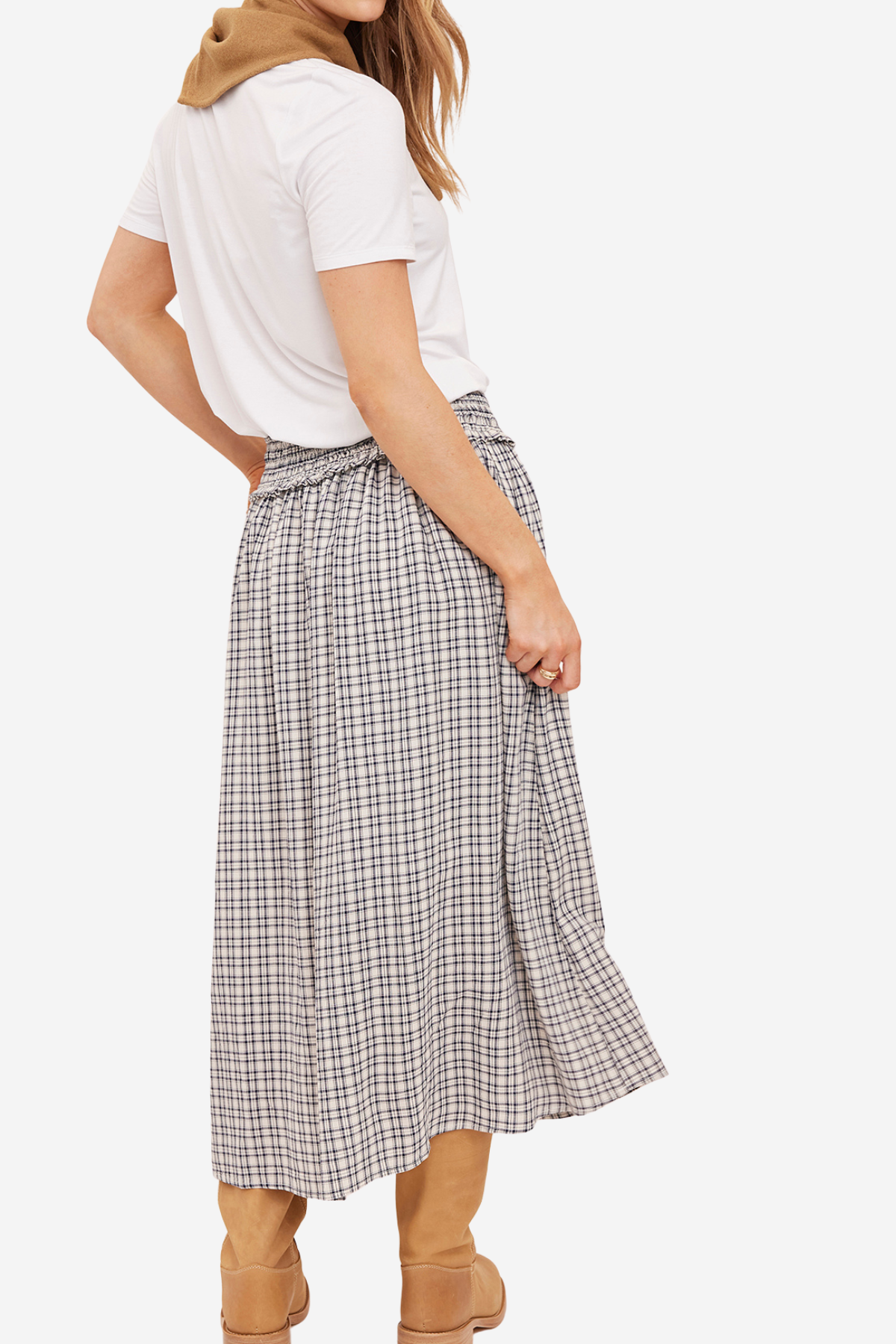 A woman shown from the back wearing a white short-sleeve top, a high-waisted beige and gray plaid midi skirt, and tan boots against a plain light background.