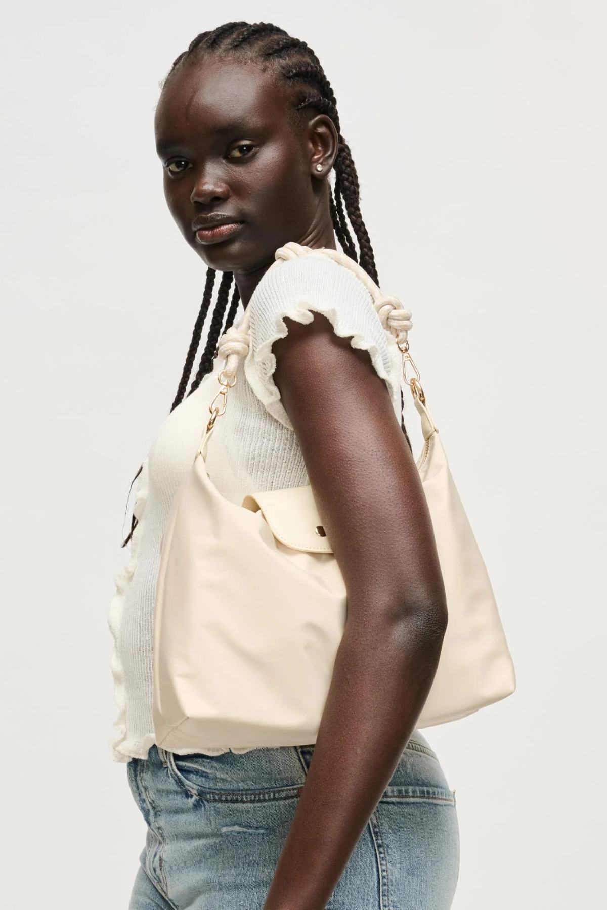 Woman wearing a beige top with ruffled sleeves and blue jeans on a white background