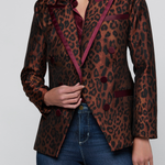 A woman wearing a brown and black leopard-print blazer with deep burgundy satin trim, paired with blue jeans, against a light gray studio background.