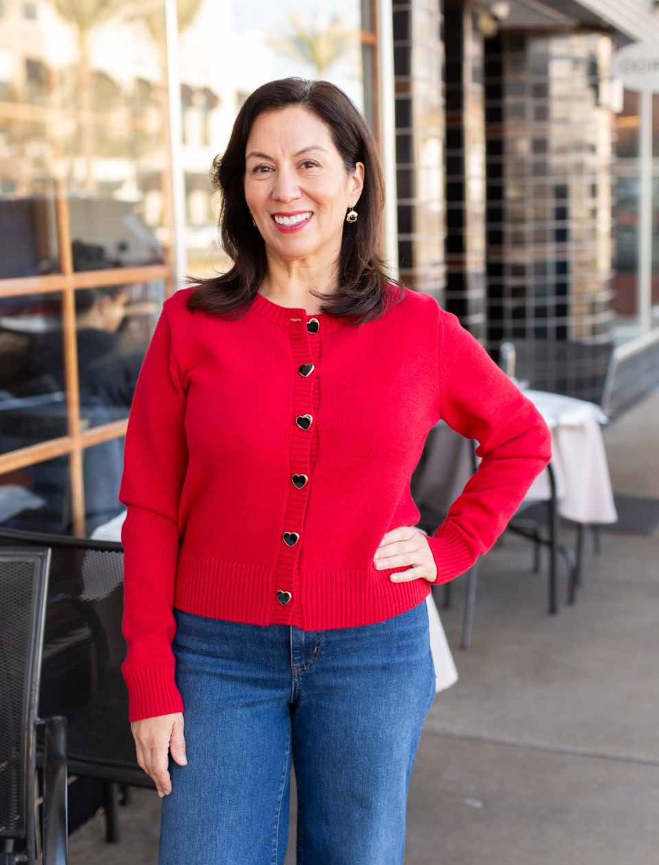 Woman wearing a red cardigan and blue jeans standing outdoors.