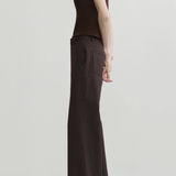 A model shown from the side in a studio setting, wearing a sleeveless dark brown mock-neck top and matching dark brown pinstriped wide-leg trousers with black pointed-toe heels.