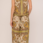 A woman shown from the back wearing a matching two-piece set with a beige, olive green, and brown paisley pattern. The set includes a short-sleeve top and wide-leg pants, photographed against a plain light beige studio background.