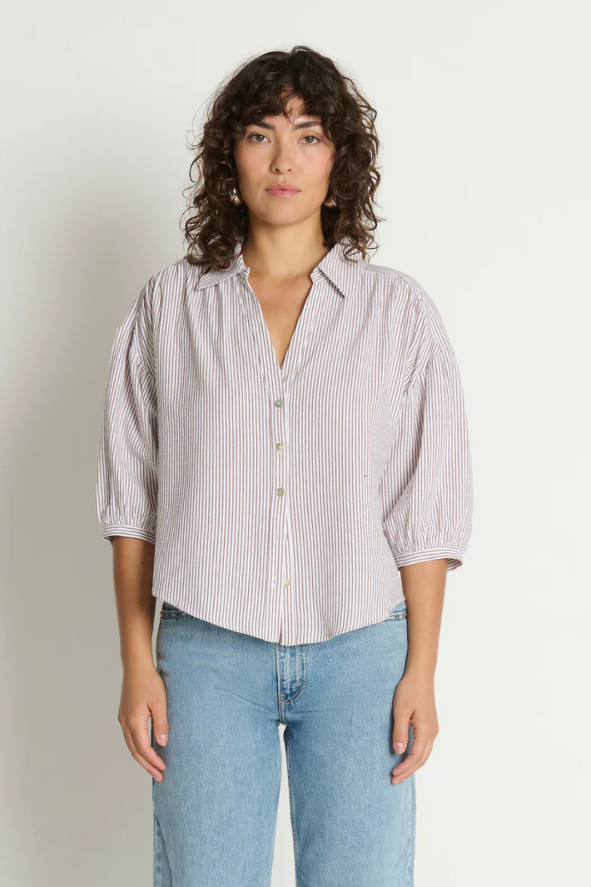 Woman wearing a striped shirt and jeans against a plain background