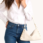 Woman wearing a white shirt and blue jeans holding a cream-colored handbag with gold accents.