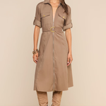 A woman models a taupe-brown short-sleeve shirt dress with a matching belt and gold buckle, styled with matching knee-high boots and sunglasses against a solid beige background.