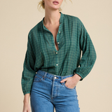 A woman modeling a green plaid button-up shirt with blue jeans against a solid beige background.
