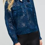 A woman wearing a dark blue sheer floral lace long-sleeve blouse with button details and black pants, photographed against a light gray studio background.