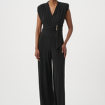A model wearing a black sleeveless wrap-style jumpsuit with a matching tie belt and a small gold accent, standing against a plain light gray studio background.