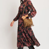 Woman wearing a patterned dress with black boots and a brown bag on a white background