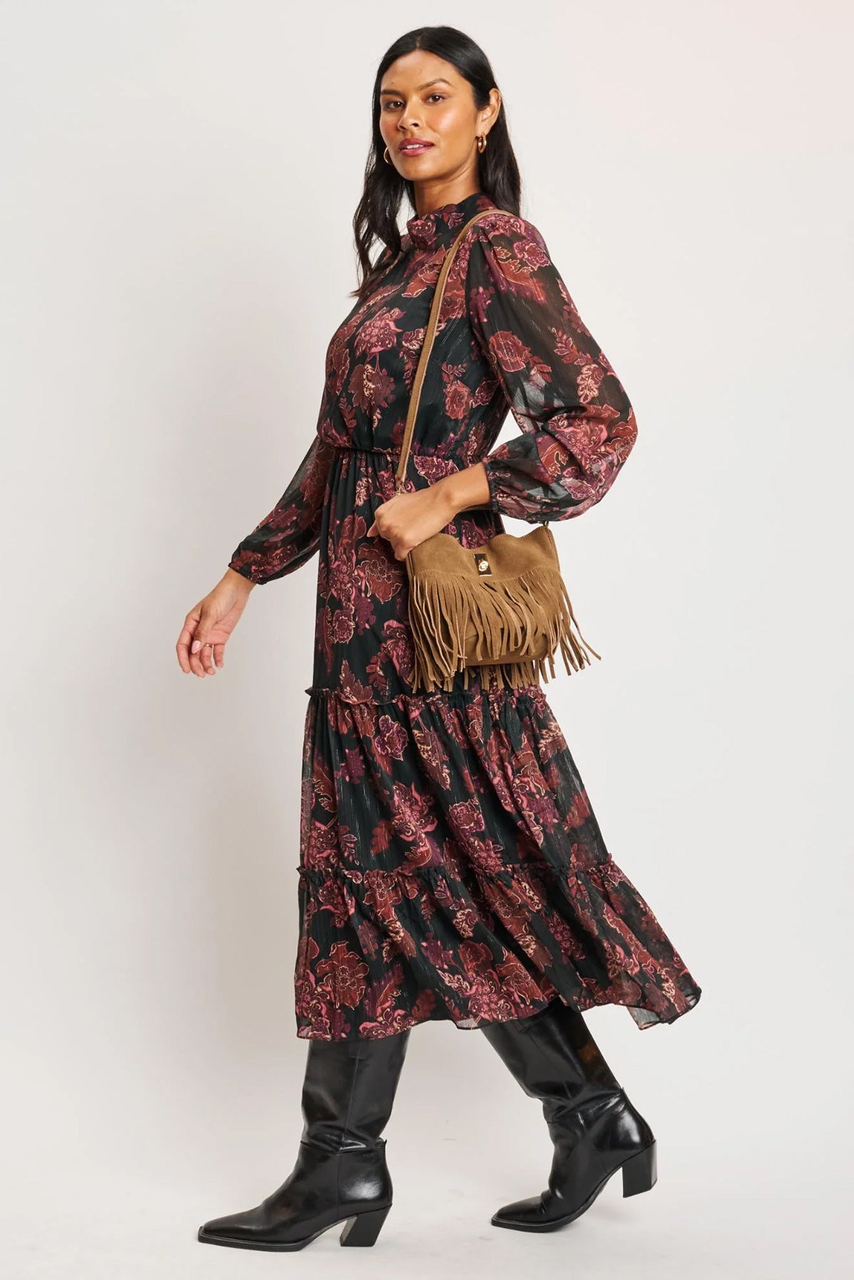 Woman wearing a patterned dress with black boots and a brown bag on a white background