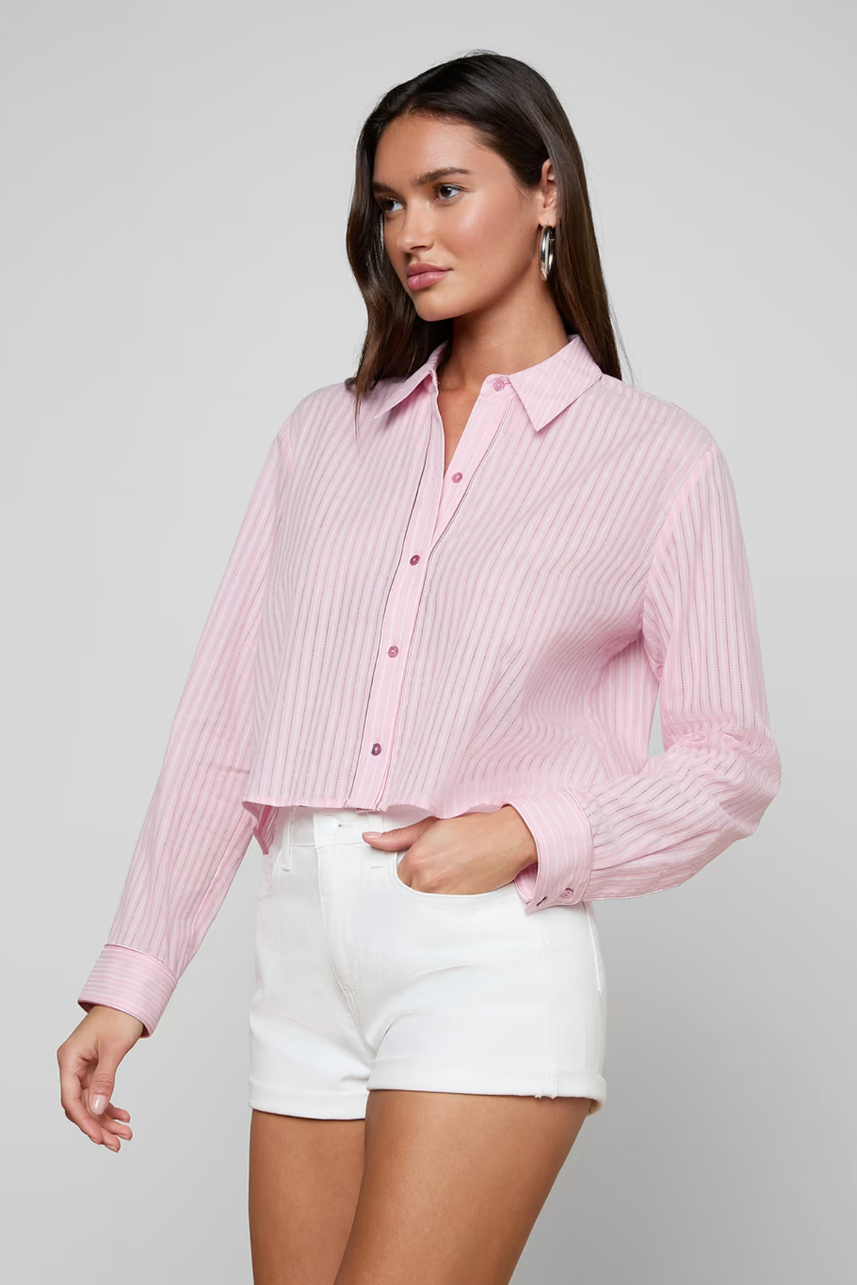 Woman wearing a pink ribbed blouse and white shorts on a gray background