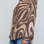 Model wearing a long-sleeve abstract print blouse in warm neutral tones paired with blue denim.