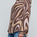 Model wearing a long-sleeve abstract print blouse in warm neutral tones paired with blue denim.