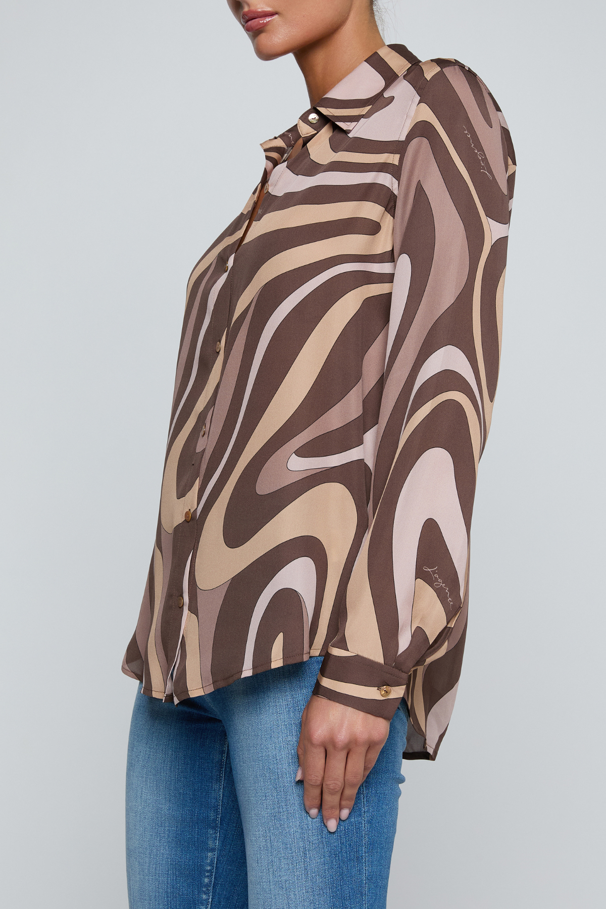 Model wearing a long-sleeve abstract print blouse in warm neutral tones paired with blue denim.