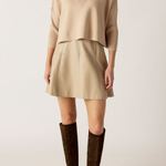 Person wearing a beige sweater and skirt with brown knee-high boots on a white background