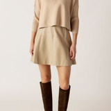 Person wearing a beige sweater and skirt with brown knee-high boots on a white background