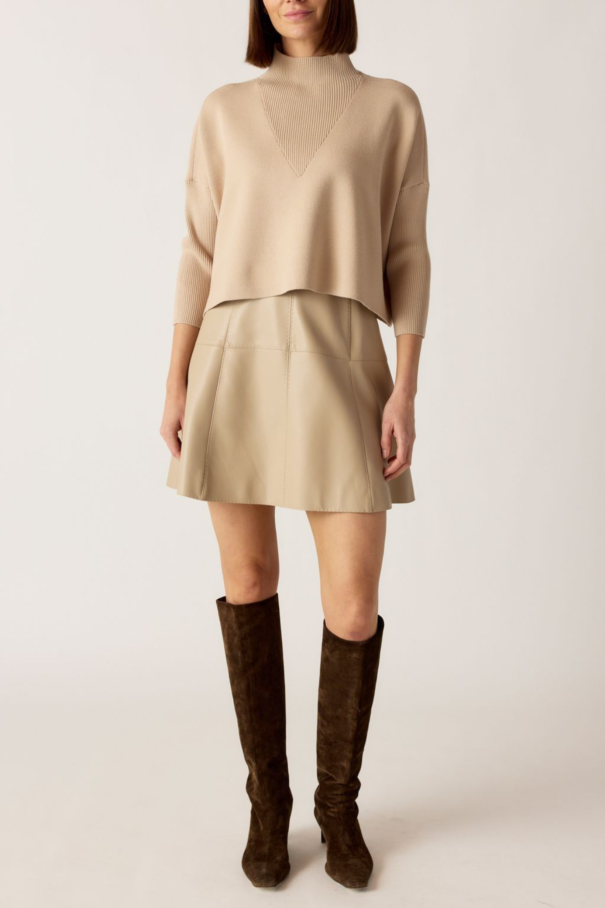 Person wearing a beige sweater and skirt with brown knee-high boots on a white background