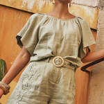 Woman in a green outfit standing against a textured wall.