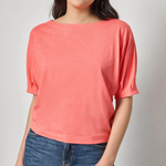 Woman wearing a coral top and blue jeans against a plain background
