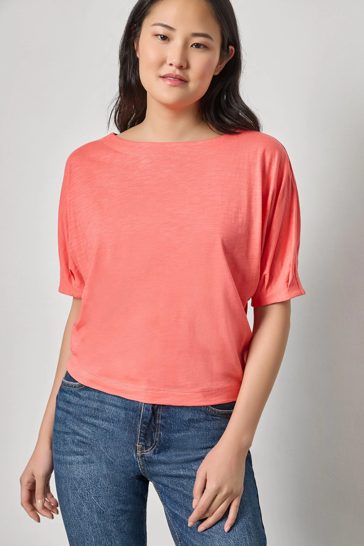 Woman wearing a coral top and blue jeans against a plain background