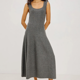 A woman modeling a sleeveless, scoop-neck, midi-length gray knit dress with a flared skirt, paired with white strappy high-heeled sandals, against a plain white studio background.
