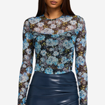 A woman modeling a sheer long-sleeve top with a blue, white, and brown floral pattern, paired with a dark navy ruched skirt, against a light gray background.