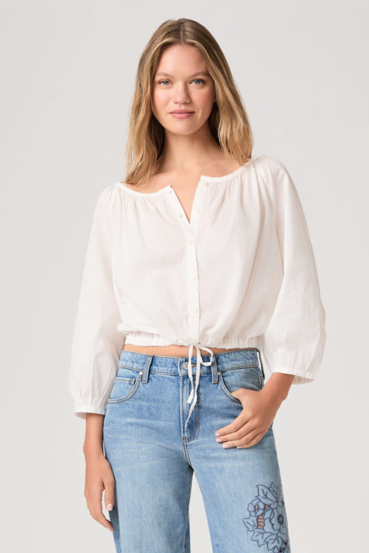 Woman wearing a white blouse and blue jeans on a plain background