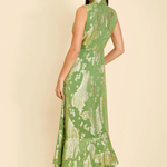 A woman modeling a sleeveless green maxi dress with a gold floral pattern, shown from the back against a solid beige background.