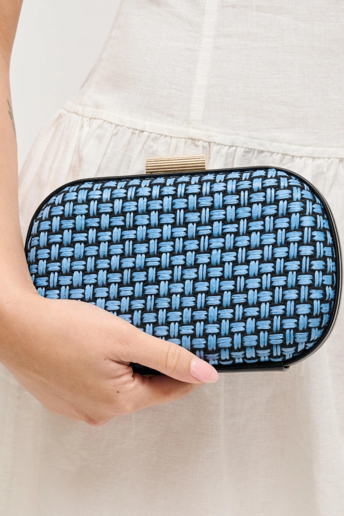 Blue woven clutch held by a person against a neutral background