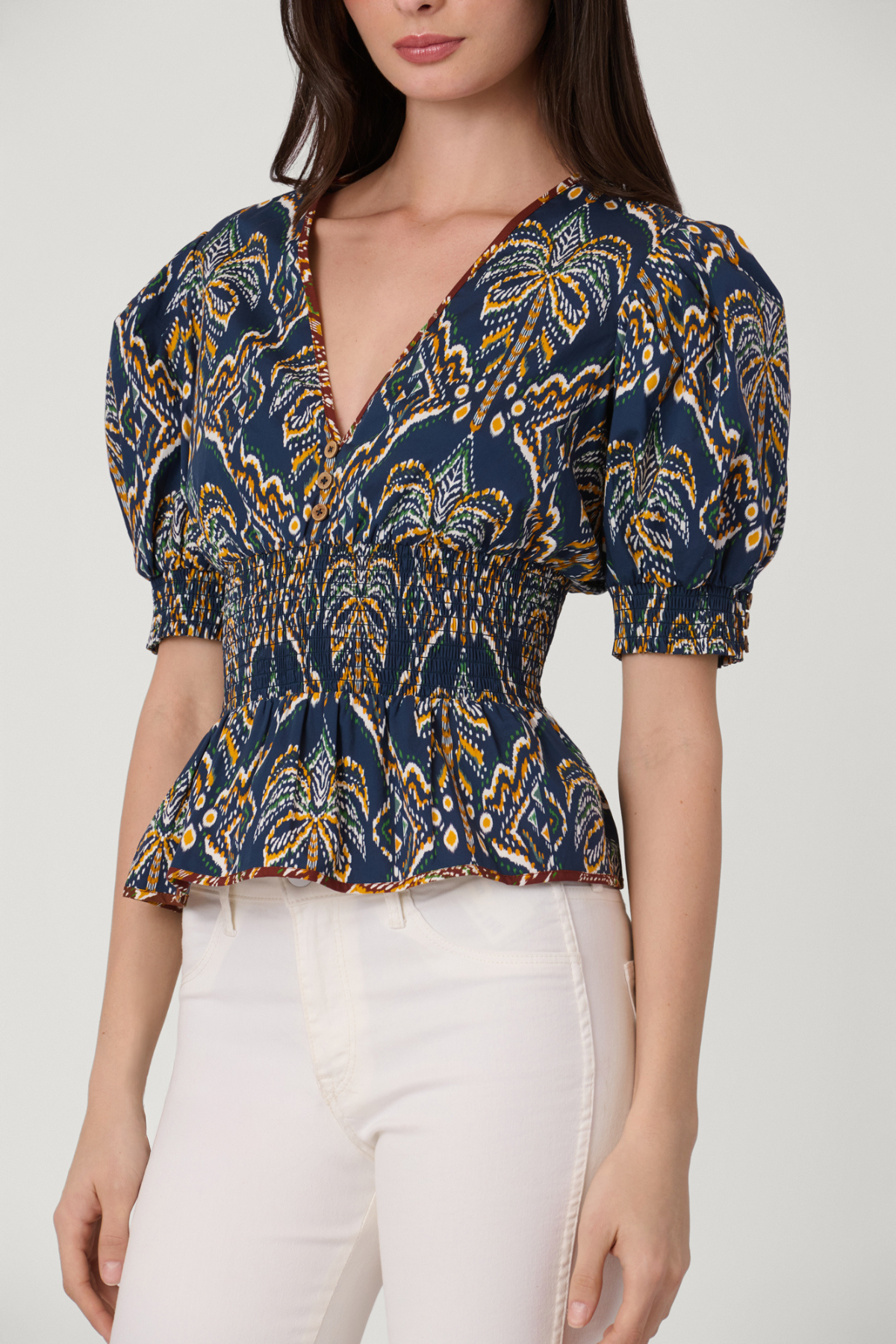 Woman wearing a patterned blue and yellow top with white pants on a plain background