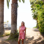Woman in a pink dress standing under palm trees on a sunny day.