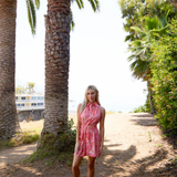 Woman in a pink dress standing under palm trees on a sunny day.