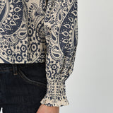 Woman wearing a patterned long sleeve blouse with a gathered neckline in neutral tones