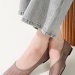Person wearing transparent sheer shoes with gray pants on a light background