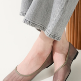 Person wearing transparent sheer shoes with gray pants on a light background