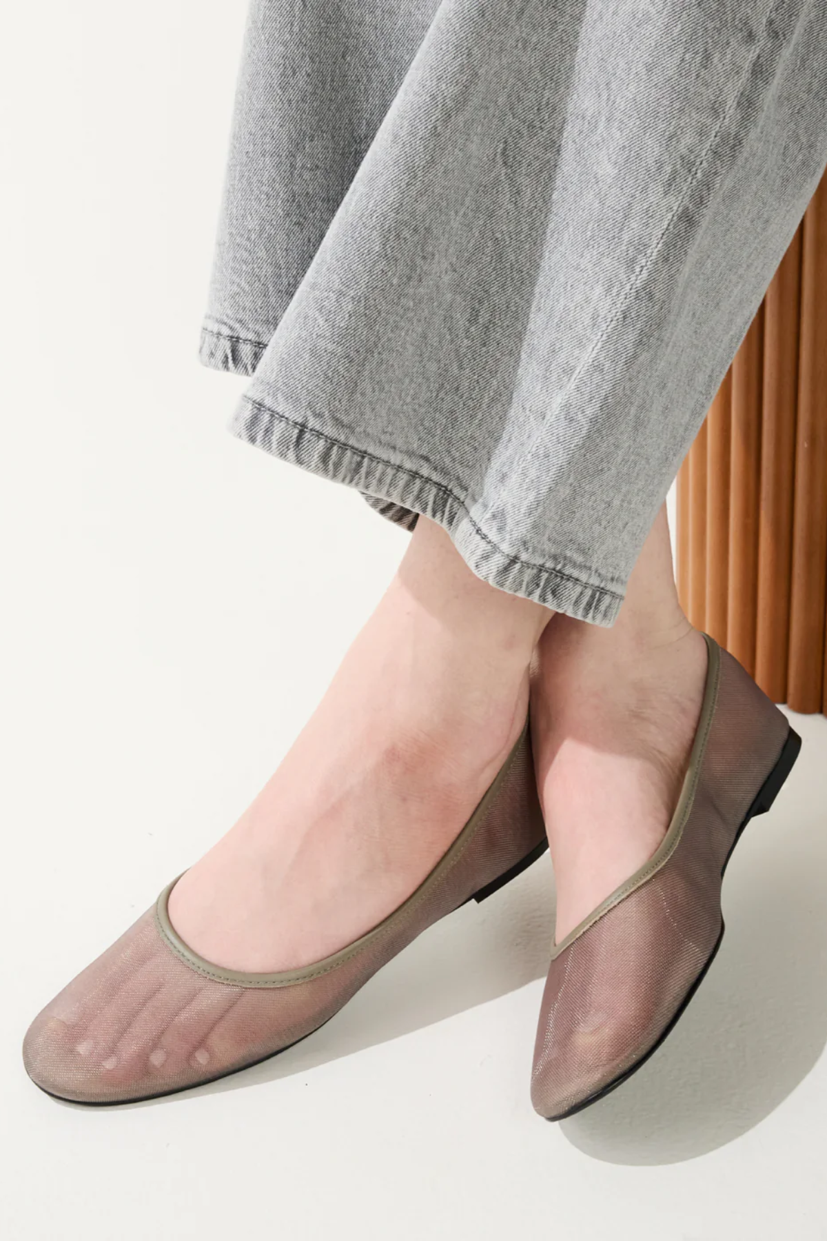 Person wearing transparent sheer shoes with gray pants on a light background