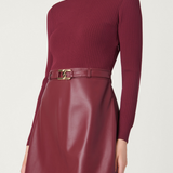 A woman wearing a ribbed long-sleeve top and a faux-leather mini skirt in burgundy, featuring a matching belt with a gold-tone buckle.