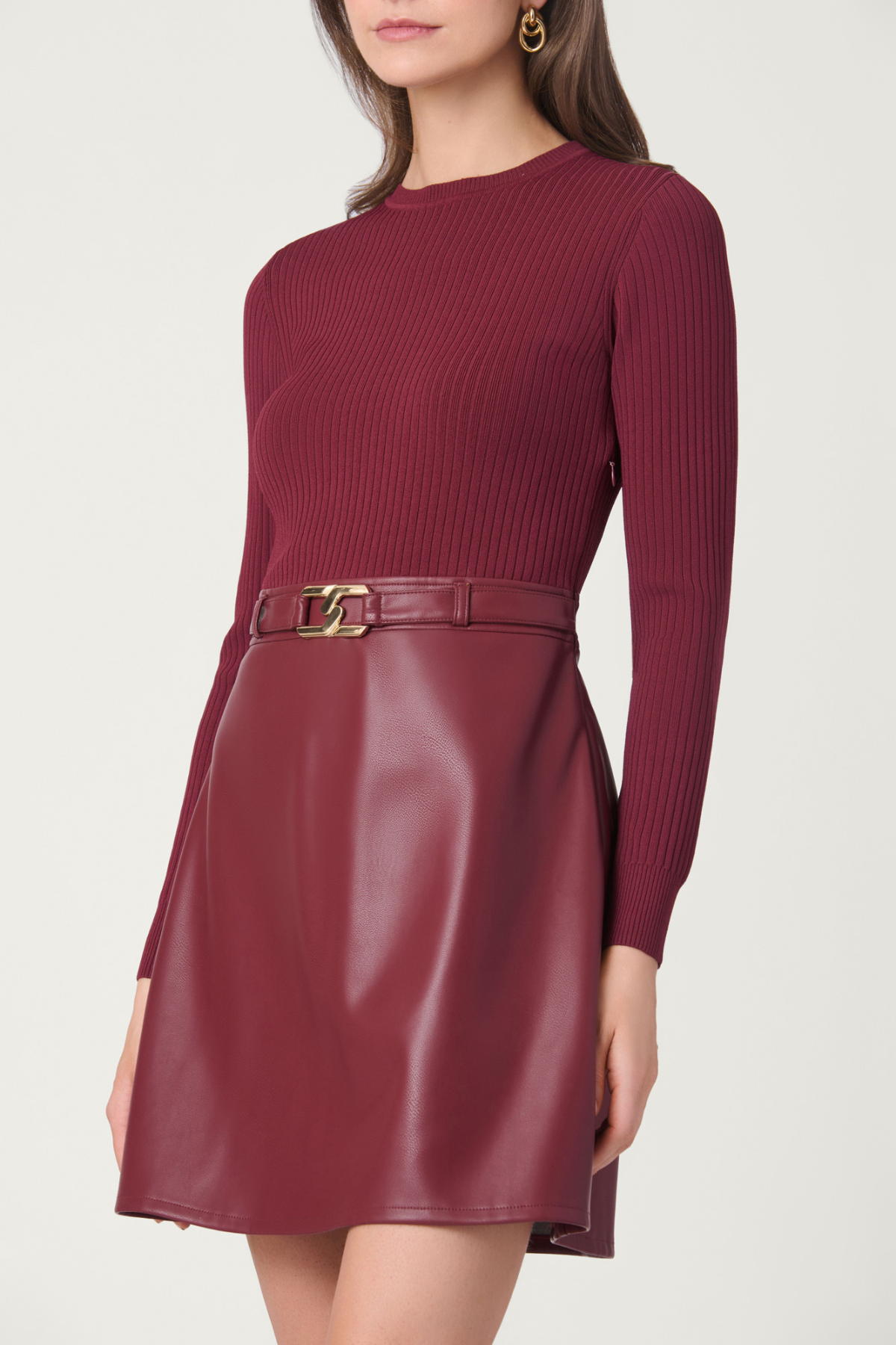 A woman wearing a ribbed long-sleeve top and a faux-leather mini skirt in burgundy, featuring a matching belt with a gold-tone buckle.
