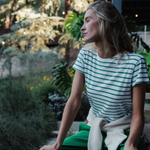 Woman sitting outdoors in a garden wearing a green and white striped shirt.