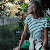 Woman sitting outdoors in a garden wearing a green and white striped shirt.