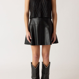 Person wearing a black sleeveless knitted top, black leather skirt, and black cowboy boots on a white background